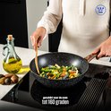 Persoon kookt een wokgerecht met groenten in een zwarte wokpan met marmerlook en houten handvat op een inductiekookplaat.