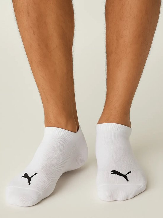 Een persoon draagt witte PUMA enkelsokken met zwart logo op de voorkant.