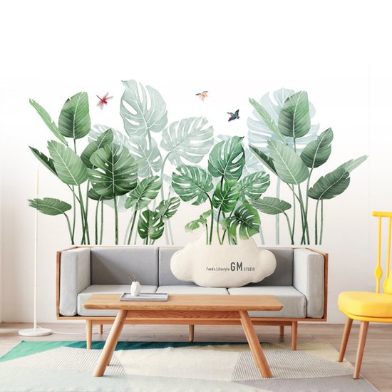 Groene palm- en monstera-bladeren met drie insecten op een witte muur, boven een grijze bank en een houten salontafel.