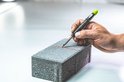Hand houdt Pica-Dry markeerstift met groene dop om te schrijven op een grijze baksteen.
