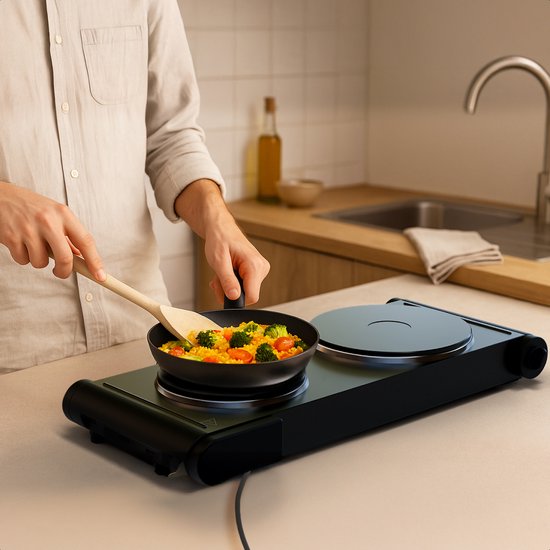 Man kookt groenten in een pan op een zwarte elektrische dubbele kookplaat in een keuken.
