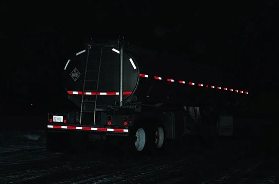 Een tankwagen 's nachts met witte en rode reflecterende tape op de zijkanten en achterkant.