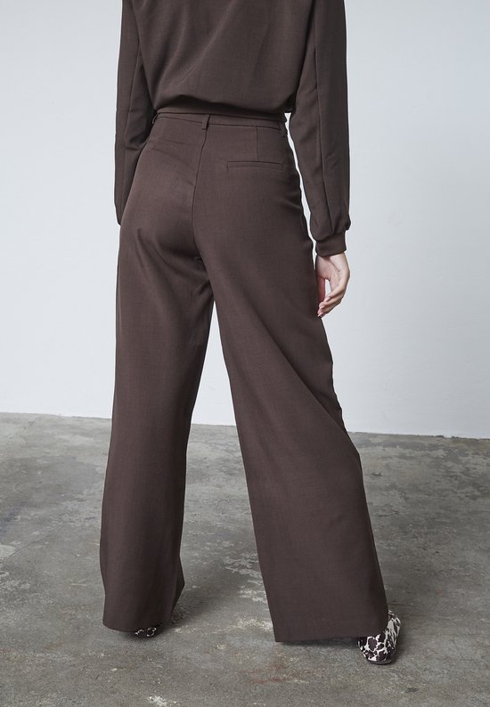 Zicht op de achterkant van een model in een bruine wijde broek en een bijpassend shirt. Schoenen met koeienprint.