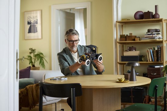 Man houdt de LEGO Icons Ford Model T vast, in een woonkamer.