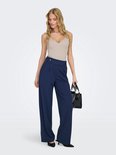 Model draagt donkerblauwe wijde broek met beige top en zwarte tas.