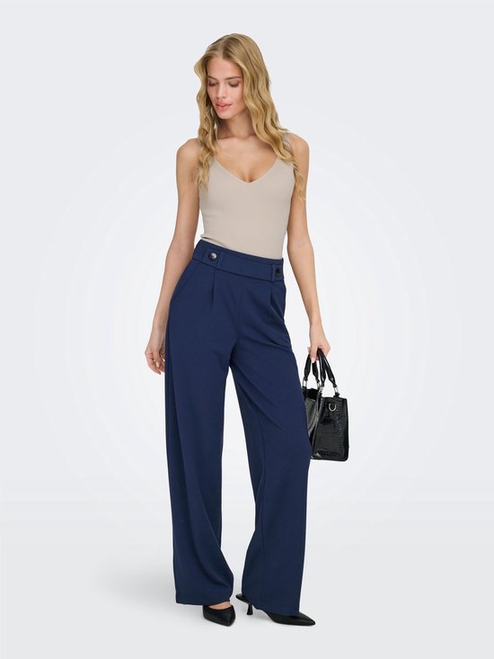 Model draagt donkerblauwe wijde broek met beige top en zwarte tas.
