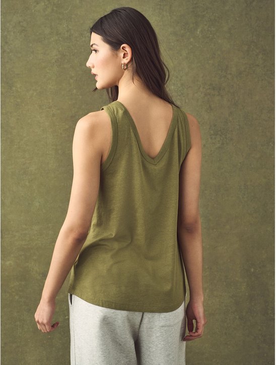 Een vrouw met bruin haar kijkt weg van de camera, draagt een groen mouwloos topje met V-hals en een grijze joggingbroek.