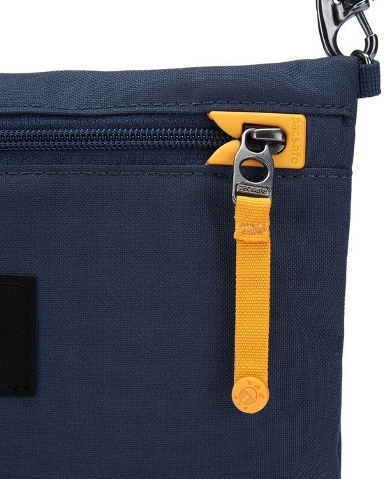 Detail van de donkerblauwe schoudertas: gele ritslip met Pacsafe logo.
