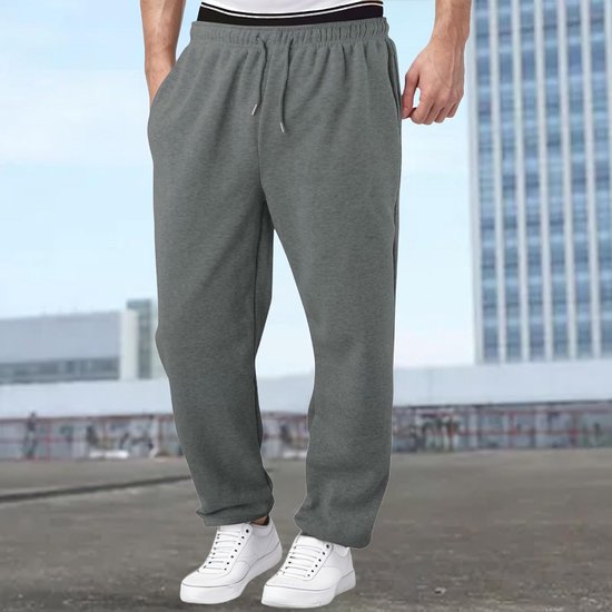 Man draagt grijze joggingbroek met trekkoord en witte sneakers, met gebouwen op de achtergrond.