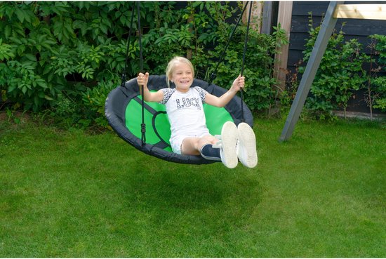 Een meisje met blond haar schommelt op een ronde, groene en zwarte nestschommel in de tuin.