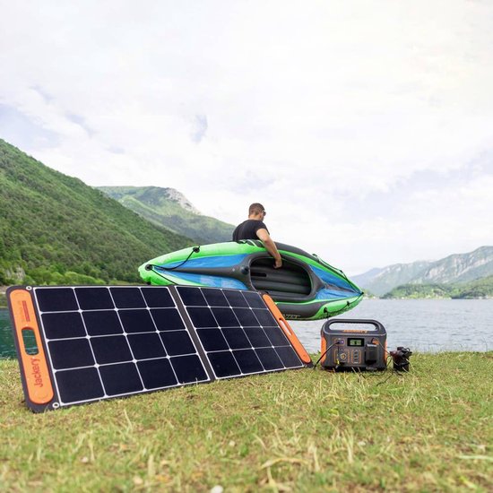 Zwart Jackery zonnepaneel en oranje Jackery solar generator op gras bij een meer, man met boot op achtergrond.