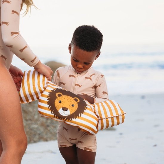 Kind met zwemband met leeuwengezicht, zittend op het strand.