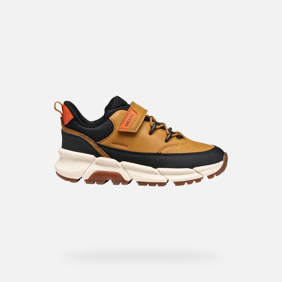 Bruine sneaker met zwarte accenten, oranje lus en klittenbandsluiting.
