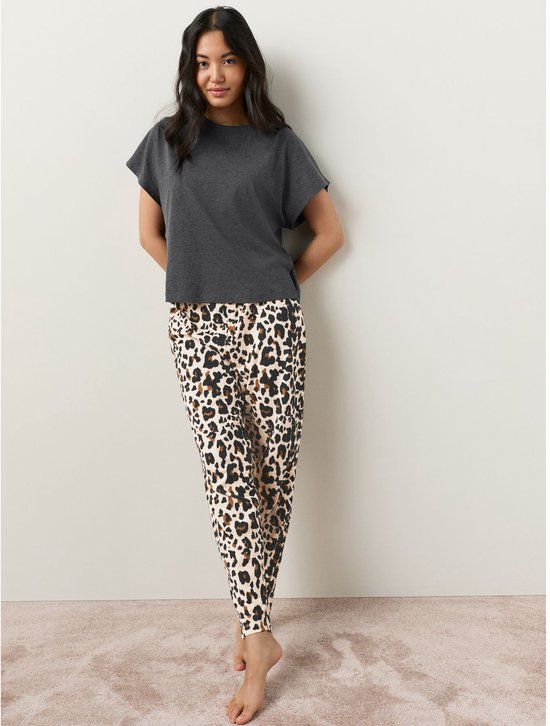 Model draagt een donkergrijs T-shirt met korte mouwen en een luipaardprint broek.