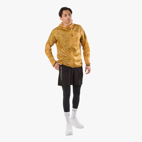 Man in geel windjack met camouflageprint, zwarte shorts en zwarte tight.