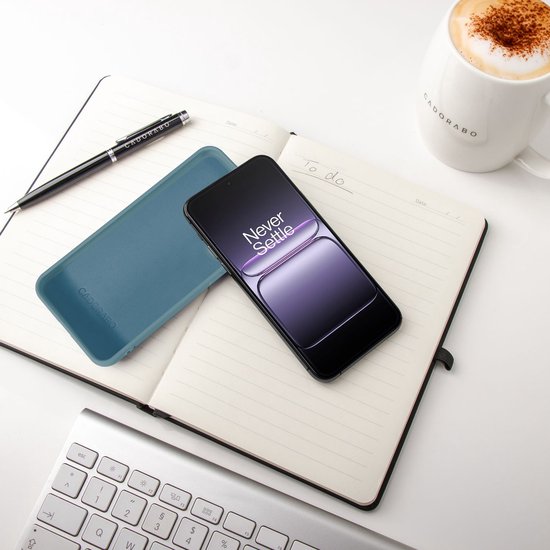 Blauw Cadorabo telefoonhoesje op een open notitieboekje, naast een smartphone en koffiemok.