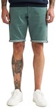 Groene slim fit stretch denim shorts met opgerolde zomen, gedragen door een model met tattoos.