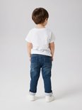 Jongen met spijkerbroek en wit T-shirt, staand van achteren.