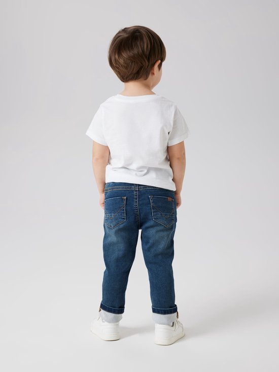 Jongen met spijkerbroek en wit T-shirt, staand van achteren.