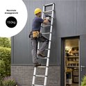 Man met gele helm en gereedschapsgordel die een Mexxo telescoopladder gebruikt bij een grijze schuur.