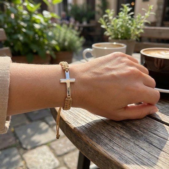 Beige gevlochten armband met zilverkleurig kruis om een damespols, in een café.