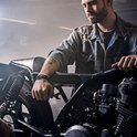 Man in werkplaats met spijkerjack, pols met zwarte leren armband met blauwe lapis lazuli kralen.