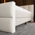 Detail van de beige boxspring met een gestreept hoofdbord en een matras met honingraatpatroon.