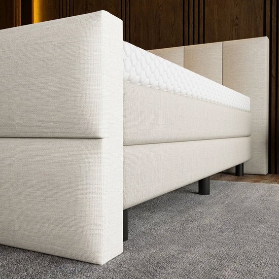 Detail van de beige boxspring met een gestreept hoofdbord en een matras met honingraatpatroon.