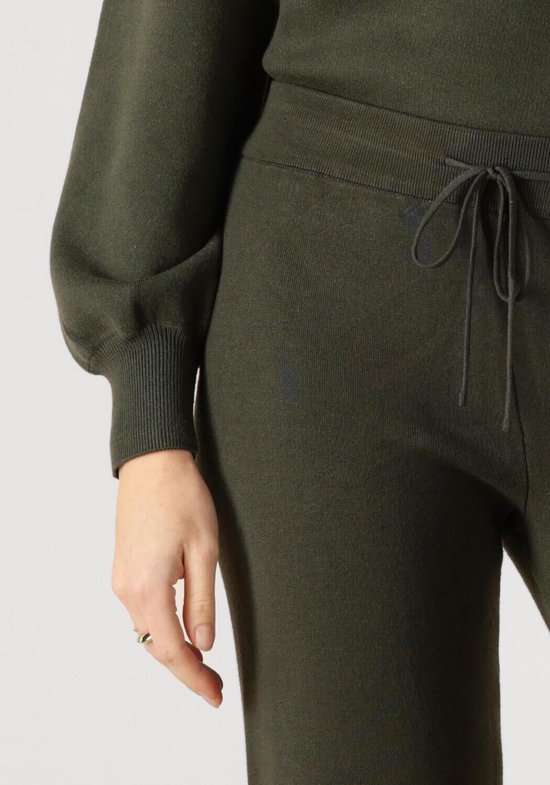 Detail van een donkergroene gebreide broek met trekkoord, aan een vrouw.