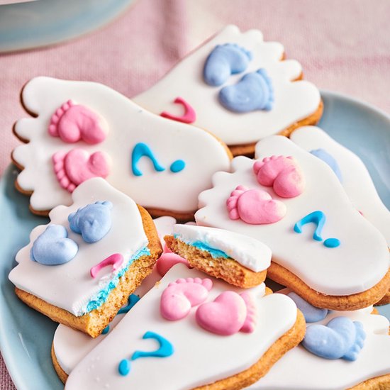 Voetvormige koekjes met witte glazuur, blauwe en roze babyvoetjes, vraagtekens en hartjes.