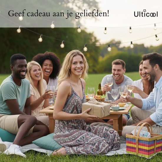 Un groupe d'amis souriants assis dehors sur une couverture, éclairés par des bougies, une femme tenant un cadeau.
