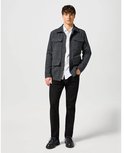 Man in donkergrijs jack, wit overhemd en zwarte jeans, staand.