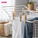 Sorbo houten wasknijpers die witte en blauwe kleding ophangen aan een droogrek. Op de achtergrond een mand.