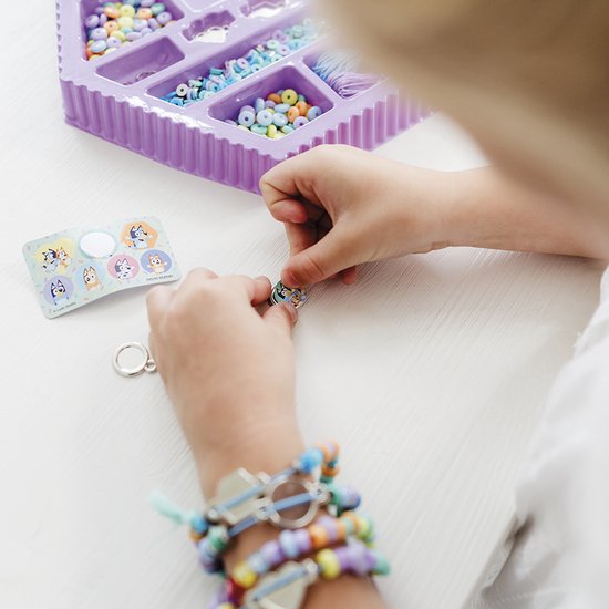 Kind maakt armbanden met paarse kralenset, met Bluey-bedels en een zelfgemaakte armband om de pols.
