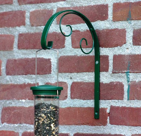 Groene metalen sierhaak bevestigd aan een bakstenen muur, met een vogelvoederhuisje eraan hangend.