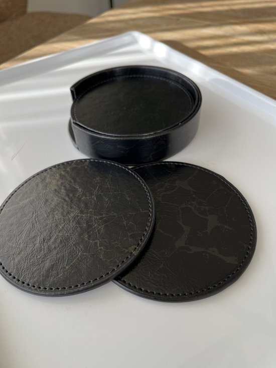 Zwarte ronde onderzetters met marmerprint, twee liggen los naast de stapel in de zwarte houder op een witte schaal.