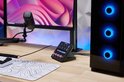 Elgato Stream Deck + op een zwarte standaard, naast een monitor en een gaming PC met blauwe verlichting.