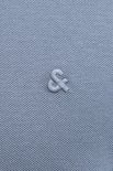 Detail van een geborduurd '&'-symbool op de borst van een blauw poloshirt.