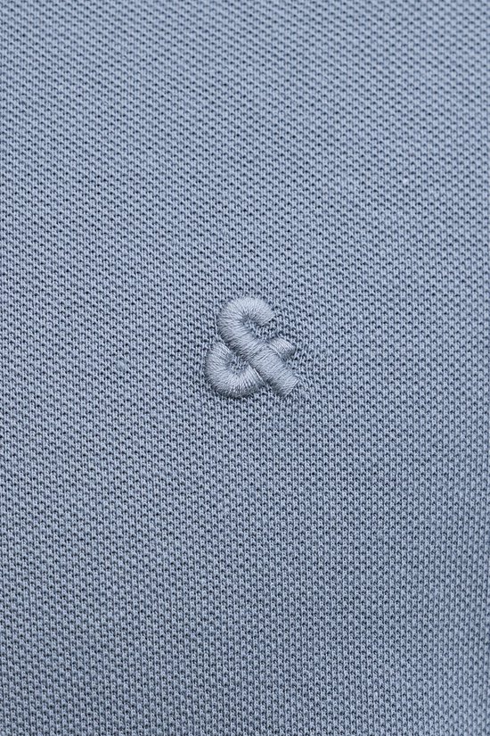 Detail van een geborduurd '&'-symbool op de borst van een blauw poloshirt.