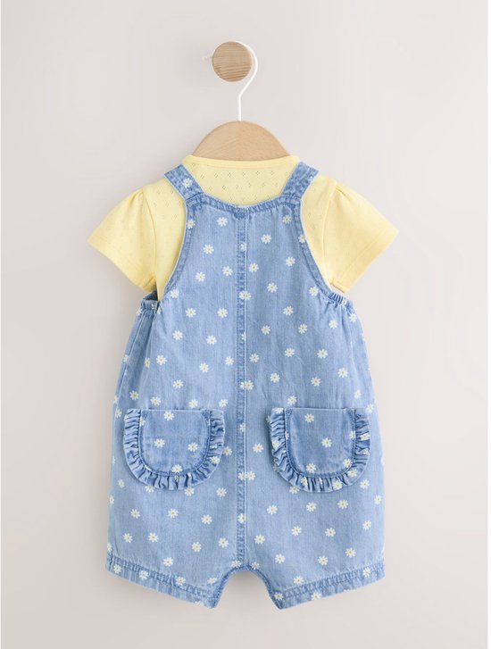 Achterkant van de set: tuinbroek met madeliefjesprint en twee achterzakken met ruches over een geel bodysuit.