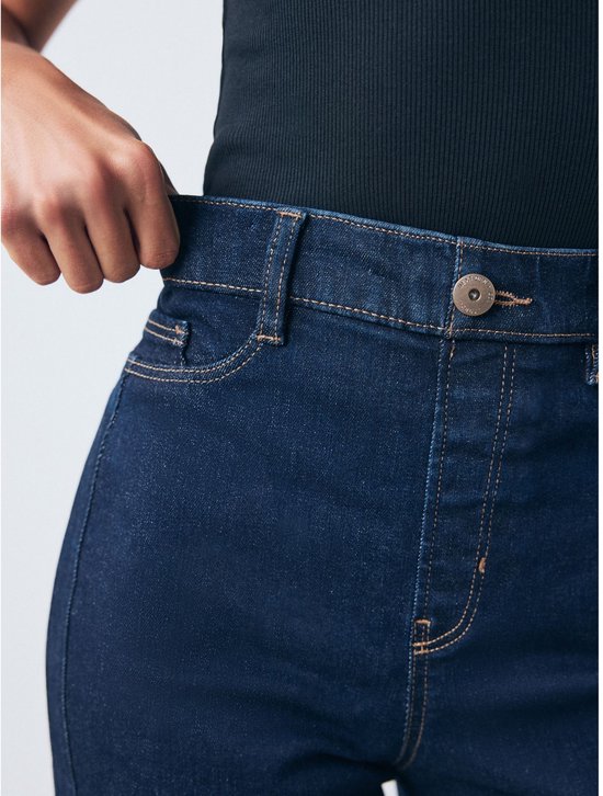 Model pakt de tailleband van een wijde, donkerblauwe spijkerbroek met hoge taille vast.