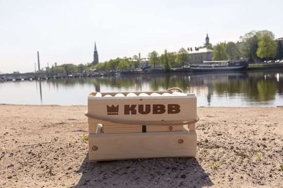Houten Kubb kistje met touw aan de zijkanten, op zand bij een meer.