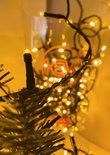 Close-up van een warme witte LED-lichtje op een takje van een kerstboom, met meer lampjes op de achtergrond.