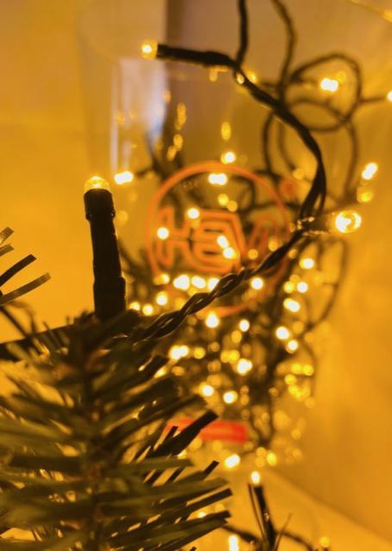 Close-up van een warme witte LED-lichtje op een takje van een kerstboom, met meer lampjes op de achtergrond.