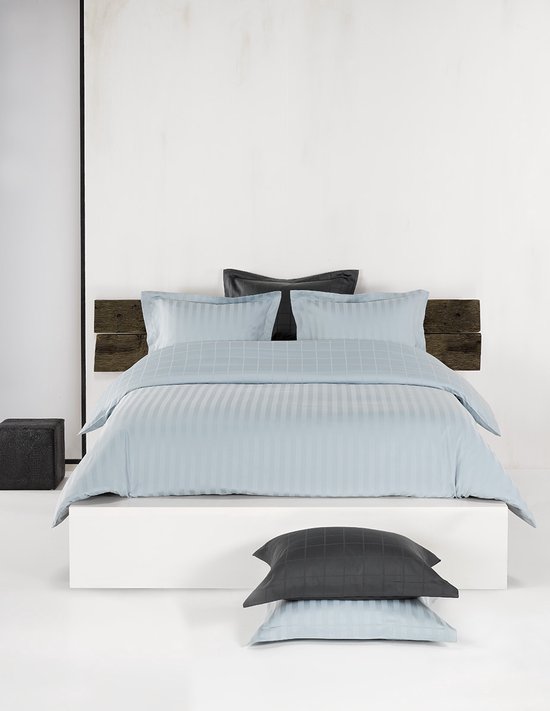 Lit fait avec une housse de couette bleu clair à rayures verticales et motif à carreaux, deux oreillers.