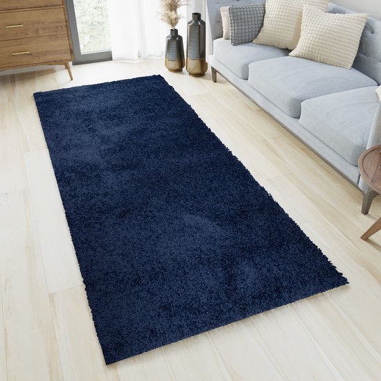 Tapis shaggy bleu foncé dans un salon, à côté d'un canapé gris et d'une commode en bois.