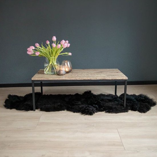 Salontafel met licht houten blad, zwart stalen frame. Boeket roze tulpen en glazen windlichten met kaarsen. Zwart schapenvachtje eronder.