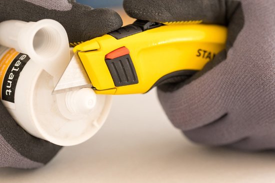 Hand met grijs werkhandschoen gebruikt geel Stanley FatMax mes om een kit koker door te snijden.