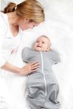 Een baby glimlacht naar een vrouw die haar met haar hand aanraakt, terwijl de baby in een grijze Swaddle UP slaapzak ligt.