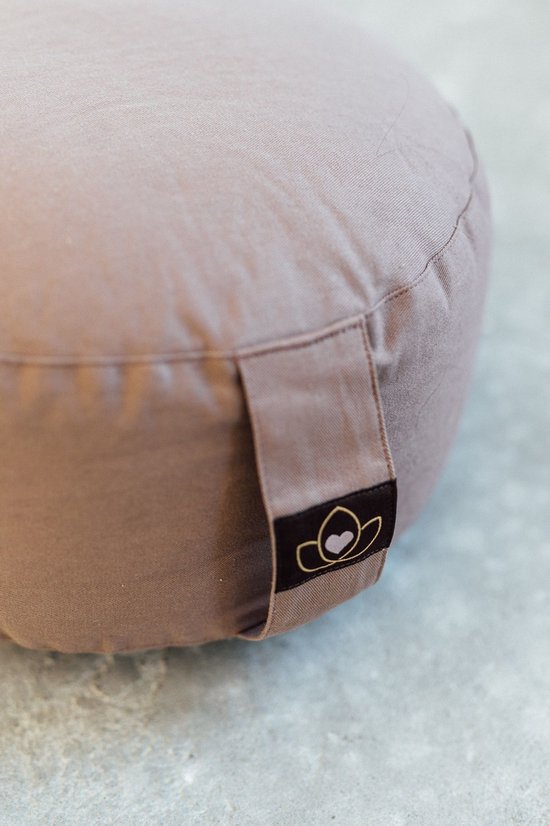 Detail van een taupe meditatiekussen met een bruin label met lotusbloem en hartje.